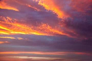 A breathtaking view of the evening sky with clouds shining red-orange shades.