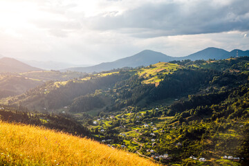 A splendid rustic scene with green rolling hills and distant huts illuminated by sunlight....