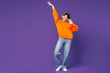 Full body young smiling cheerful happy woman she wear orange hoody casual clothes listen to music...