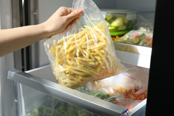 Woman taking plastic bag with frozen yellow beans from refrigerator, closeup