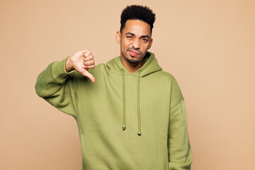 Young sad upset man of African American ethnicity wear green hoodie casual clothes showing thumb down dislike gesture isolated on plain pastel light beige background studio portrait Lifestyle concept