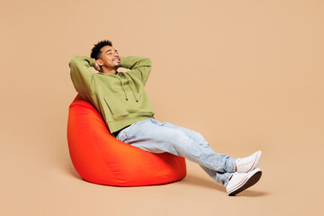 Full body young man of African American ethnicity he wears green hoodie casual clothes sit in bag...