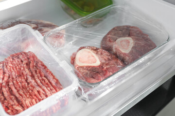 Frozen beef steaks and minced meat in containers on fridge shelf, closeup