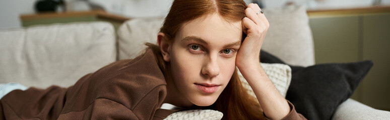 A handsome young man with long red hair enjoys a laid-back moment in his stylish apartment, banner