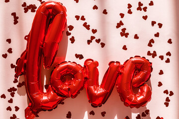 Valentines flat lay. Stylish red love shaped balloon and red hearts confetti on pink background in...