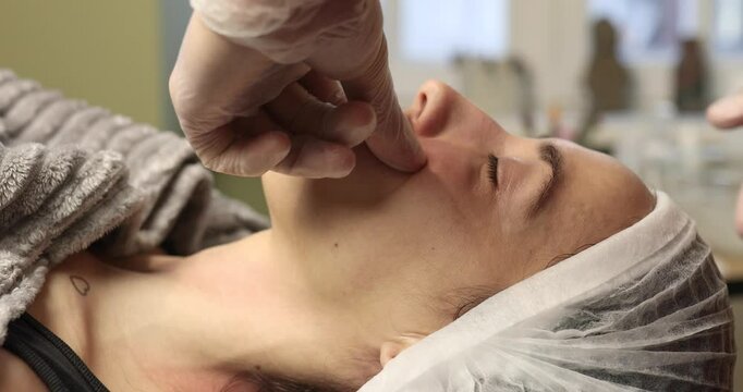 A man is massaging a woman's face. The woman is smiling and she is enjoying the massage. The man is wearing gloves, which suggests that he is taking precautions to maintain hygiene during the massage
