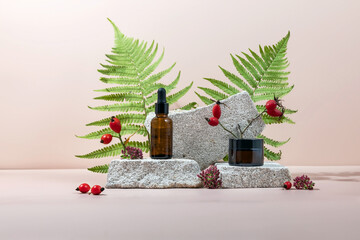 A dropper bottle with vitamin C and whey oil and a jar of hand or face cream on a podium made of stone and rosehip fruits. Anti-aging antioxidant cosmetic serum with vitamin C, natural cosmetics.