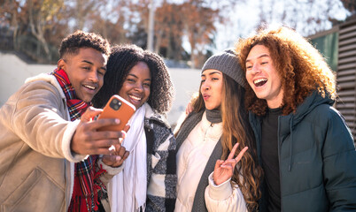 Four cheerful multi-ethnic young students taking a selfie outdoors in winter