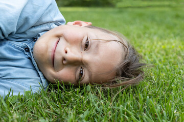 close-up of the cute face of an 8 year old boy lying on the grass. joy of childhood, positive. Hello summer, energy of nature. Earth Day