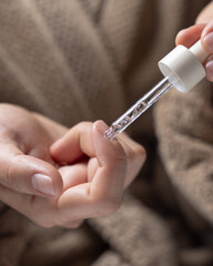 Woman in brown bathrobe dropping cuticle oil on a fingernail and holding a pipette closeup