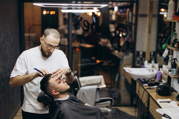 Obraz premium a photo of a professional barber focusing on the work of a client in a barber chair in front of a mirror in a modern barbershop