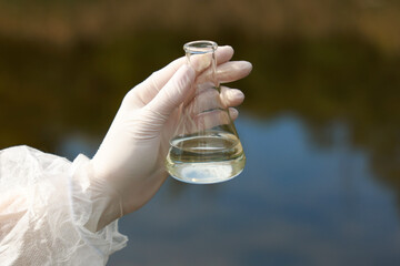 Examination of water quality. Researcher holding flask with sample outdoors, closeup