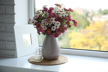 Beautiful flowers in vase and candle near window at home