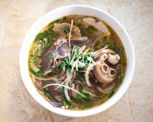 Top view cooked trotters in traditional Bun Bo Hue noodles paired with tender slices of beef,...