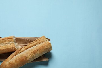 Paper bag and fresh baguette on light blue background, top view. Space for text