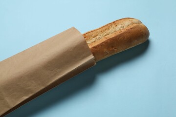 Paper bag with fresh baguette on light blue background, above view