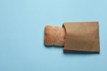 Paper bag with fresh ciabatta on light blue background, top view. Space for text
