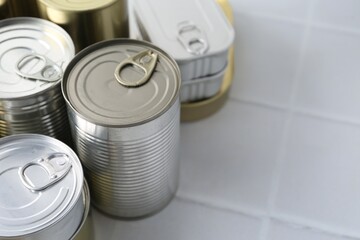Many closed tin cans on white tiled table, closeup. Space for text
