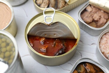 Open tin cans with different preserved products on white table, closeup