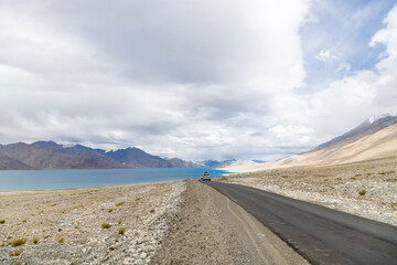 Himalayan mountain view of a car driving a scenic road along the Pangong Tso Lake, Leh, Ladakh, India.