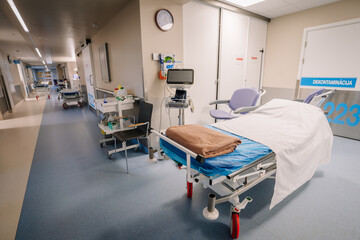 A clean hospital hallway with a medical bed, monitoring equipment, chairs, and supplies. Bright and...