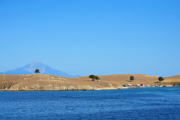 Calm sea, sand coast with 4 trees silhouetting distant mountains of Athos ,Greece 