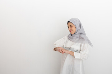Muslim woman in a light-colored hijab and dress contemplating against a minimalist white...