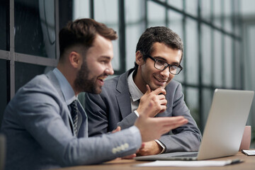 Fototapeta premium Two young businessmen sitting at workplace and working together in office