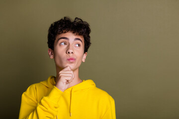 Young teenager in a yellow hoodie pondering thoughtfully against a khaki backdrop