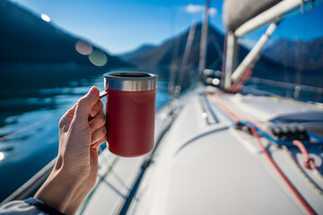Woman hands holding thermo mug sitting on bow of the yacht during sailing in the morning in winter time in Adriatic sea, relaxation in yachting time