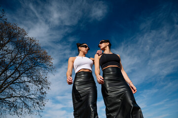 Two stylish women walking confidently under sunny skies, blending modern elegance with bold...