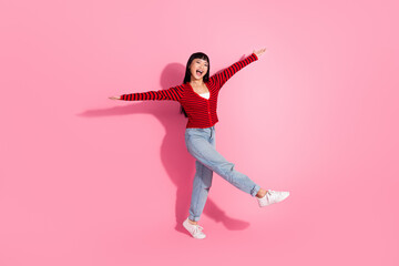 Happy young woman dancing joyfully against a pink background in casual clothing