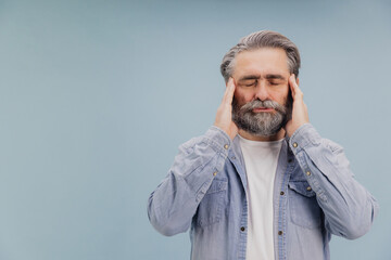 Senior man suffering from headache touching temples with closed eyes on blue background