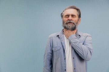 Senior man suffering from sore throat touching neck with hand on blue background