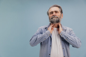 Senior man suffering from sore throat touching neck with hands on blue background