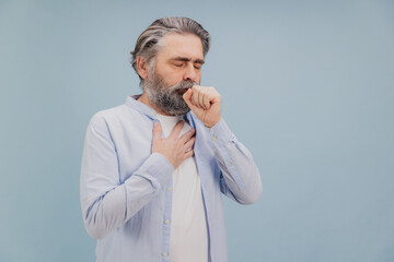 Senior man suffering from cough and chest pain on blue background