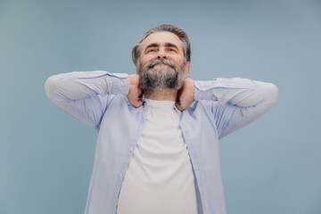 Senior man holding neck and stretching against blue background