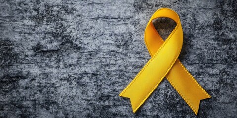 Yellow awareness ribbon placed diagonally on textured grey background with a subtle shine and shadow highlighting the ribbonâ€™s curves and edges.