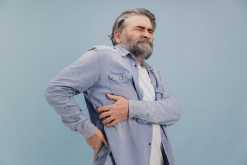 Senior man suffering from back pain on blue background