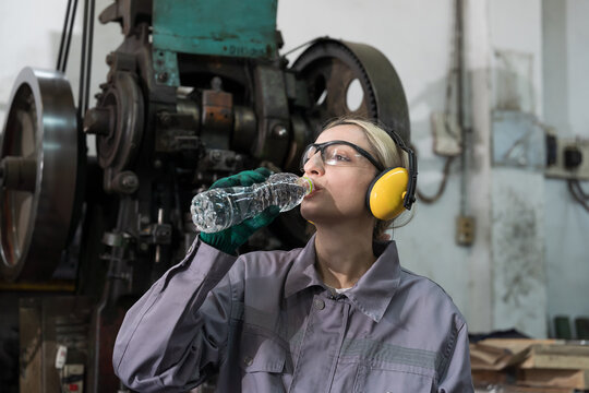 Woman engineer drinking water in break time in factory. Woman worker working and wearing safety uniform, helmet in industry factory