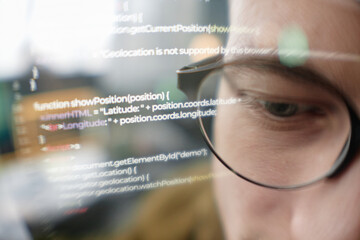 Extreme close up of male IT programmer wearing glasses looking at computer screen with lines of...