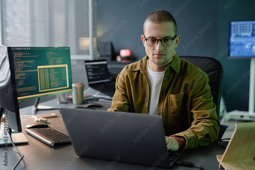 Poster medium shot of male computer programmer immersed in coding on laptop while sitting at neatly organiz