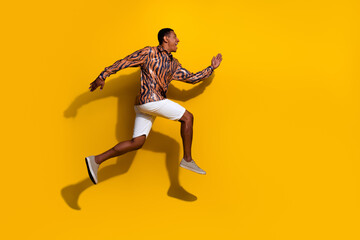 Young man in vibrant tiger-print shirt jumping against bright yellow background showcasing summer energy