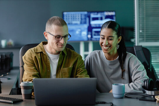 Medium shot of smiling female IT programmer at work meeting with cheerful male colleague using laptop collaboratively at desk in modern office