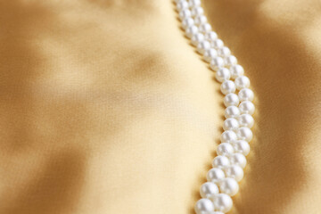 Beautiful pearl necklace on golden silk, closeup. Space for text