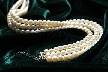 Beautiful pearl necklace on green cloth, closeup