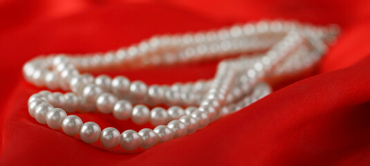 Beautiful pearl necklace on red silk, closeup