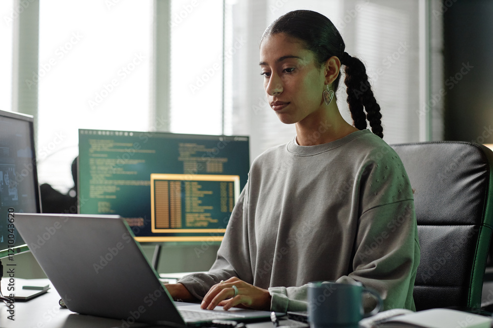 Poster medium shot of middle eastern female programmer coding on laptop sitting at professional workstation