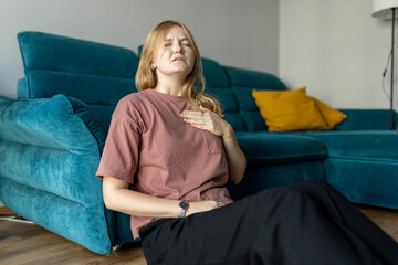Woman sitting with strong chest pain and hand touching her chest while having trouble at home....