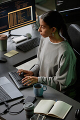 High angle of young Middle Eastern female programmer immersed in coding on keyboard of desktop PC,...